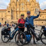 Pareja con bicicletas eléctricas y la Compostela frente a la Catedral de Santiago